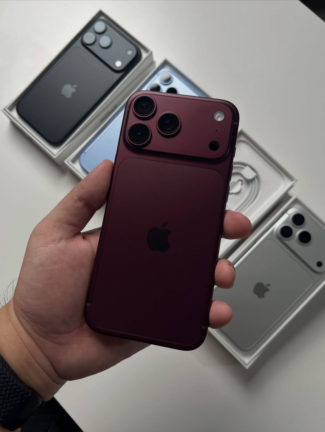 Burgundy iPhone 18 Pro Max held in one hand on launch day, retail boxes behind it